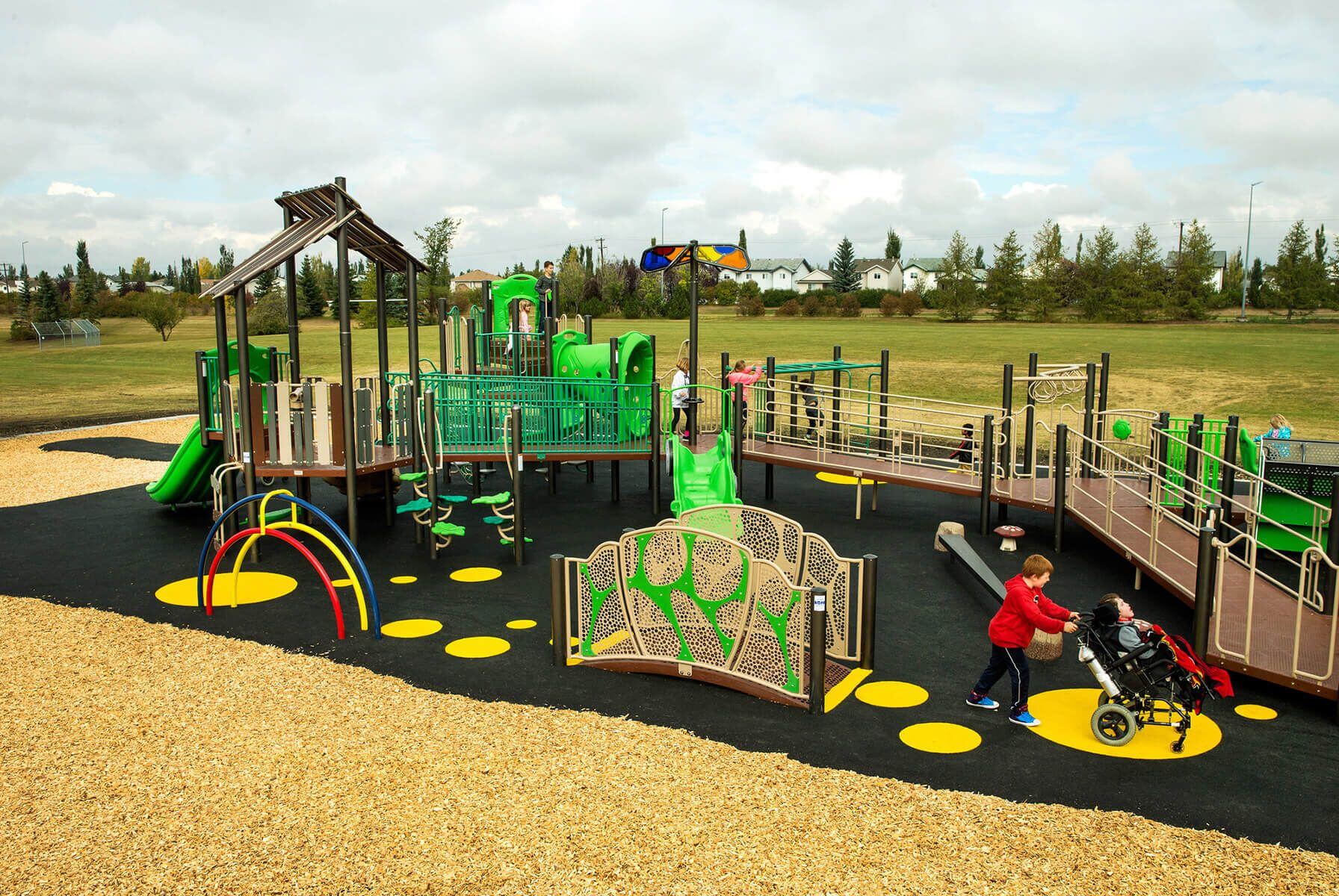 Inclusive playground featuring ramps, sensory panels, and accessible surfacing, with children of all abilities playing together in a large, open park setting.
