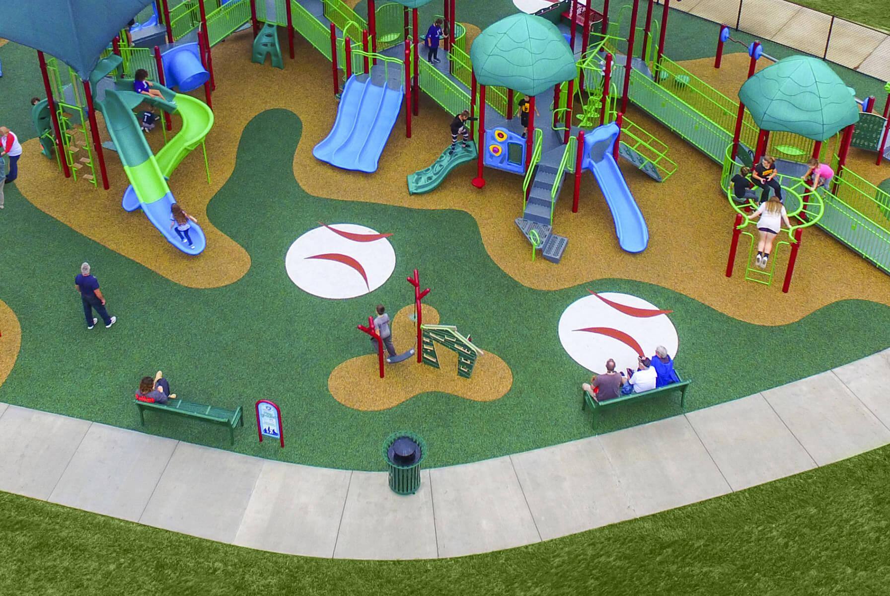 Aerial view of a large, baseball-themed inclusive playground featuring colorful slides, ramps, and accessible surfacing, with children and adults actively playing and relaxing.