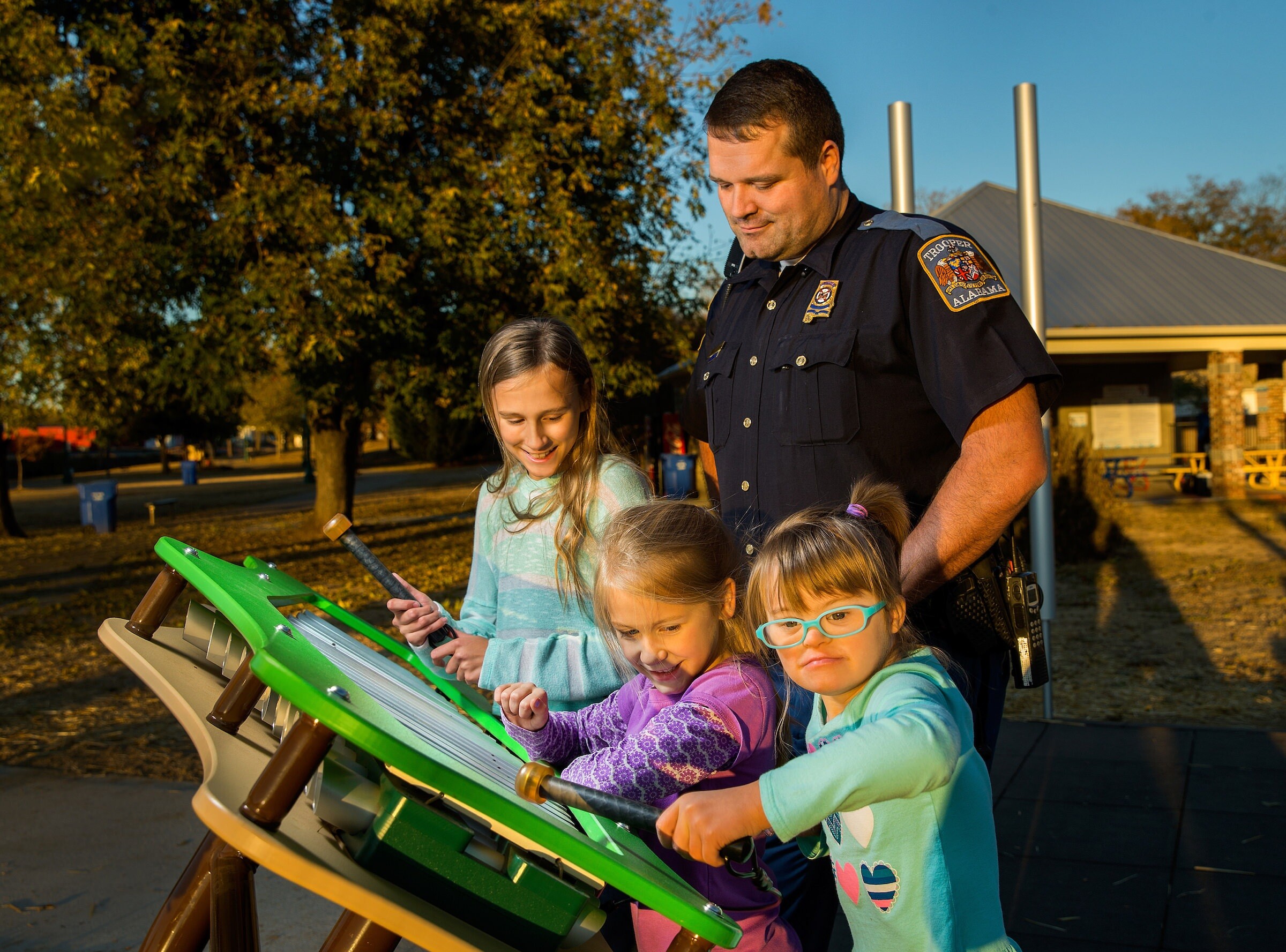 An Alabama State Trooper observing three children playing with a xylophone installation at a park