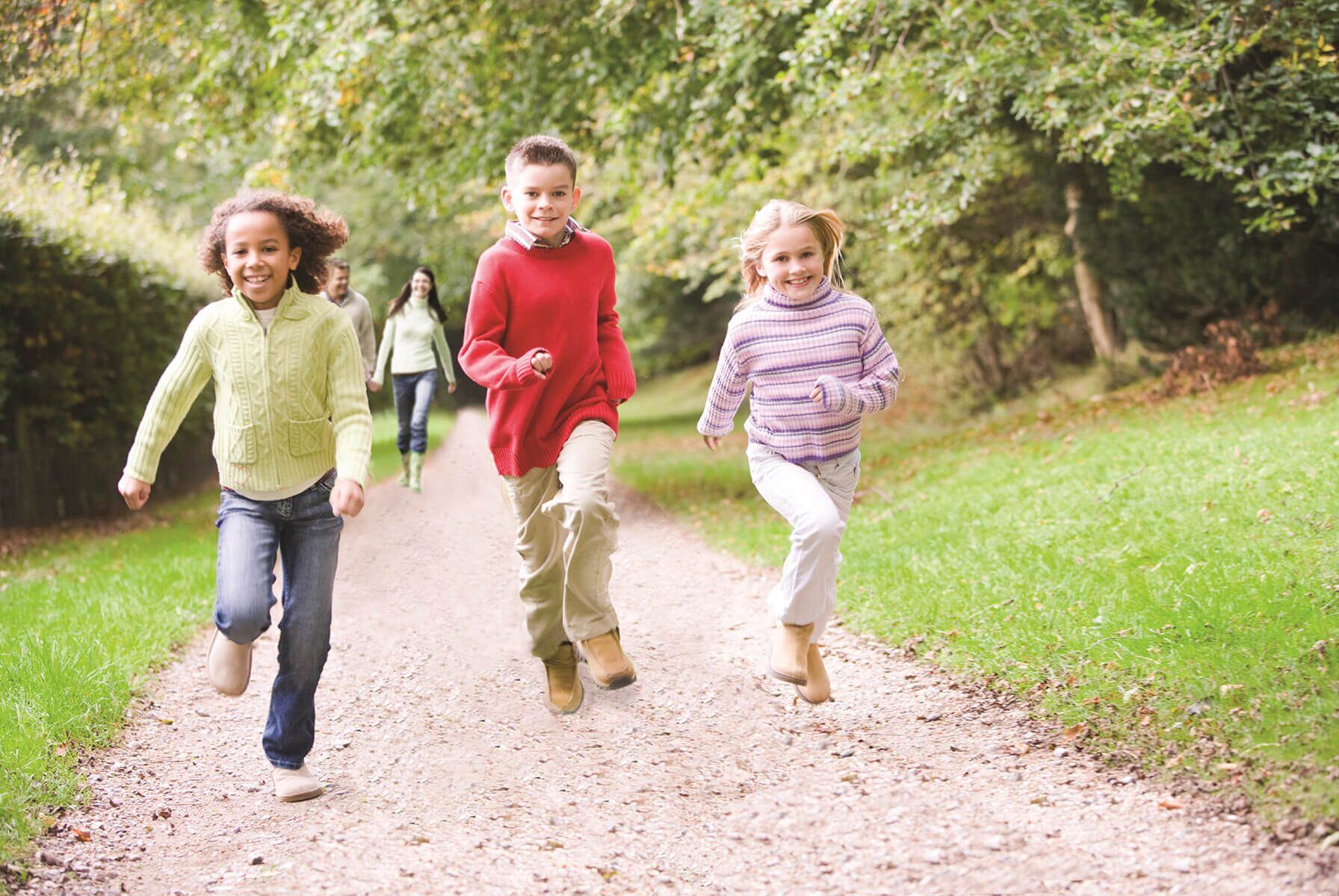 Children running on wooded trail with parents behind.