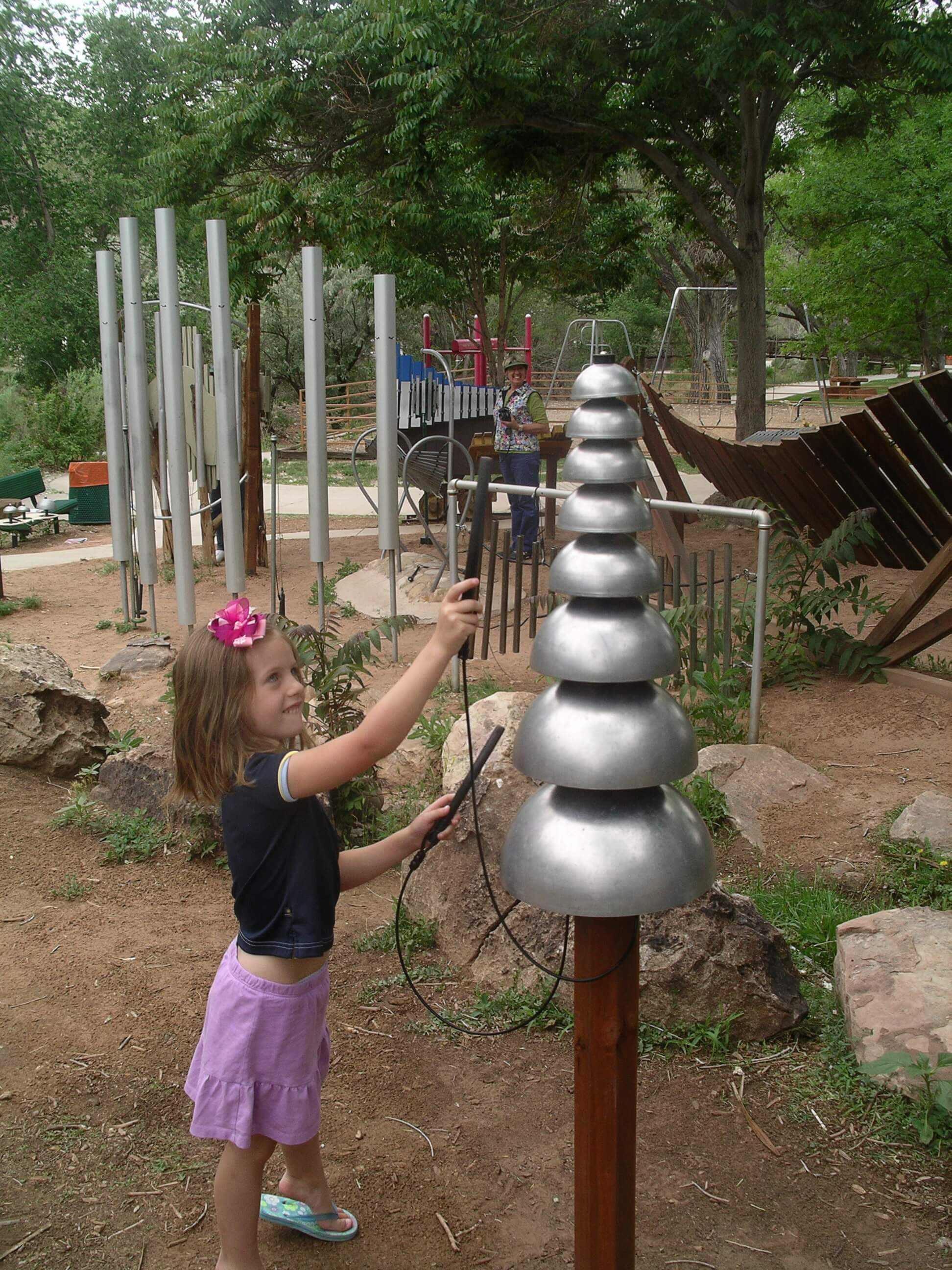 Girl playing metal percussion instrument at outdoor music playground.