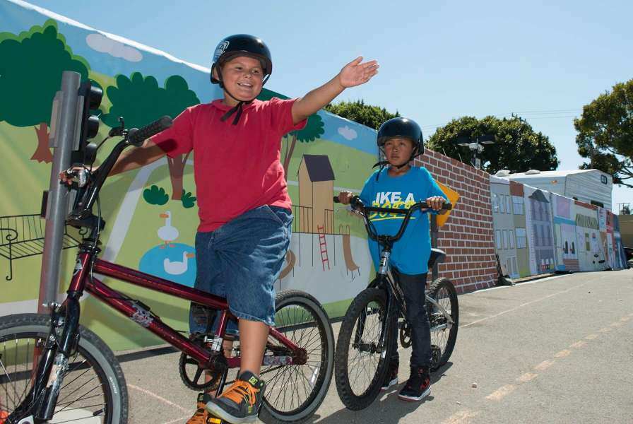 Two helmeted children riding bicycles in front of an urban mural