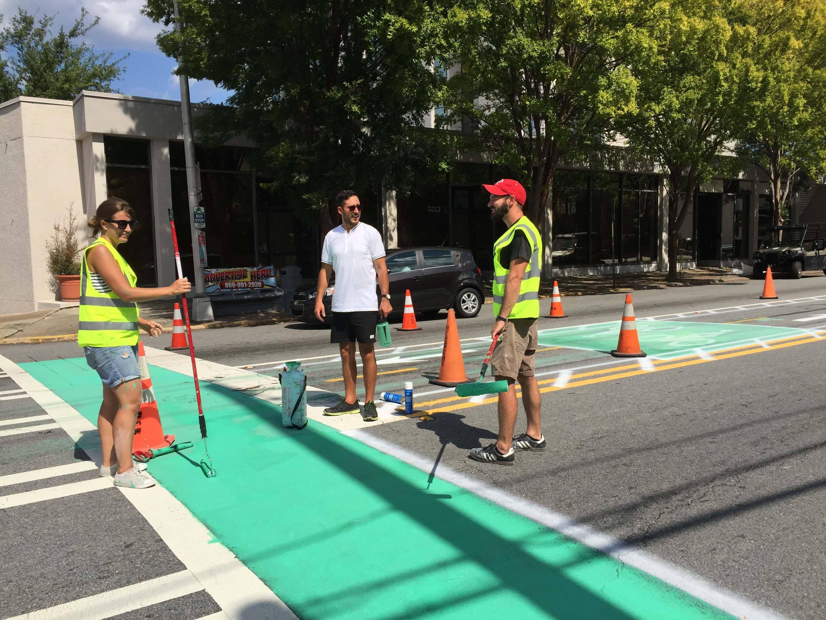 Volunteers painting green bike lane on city street.