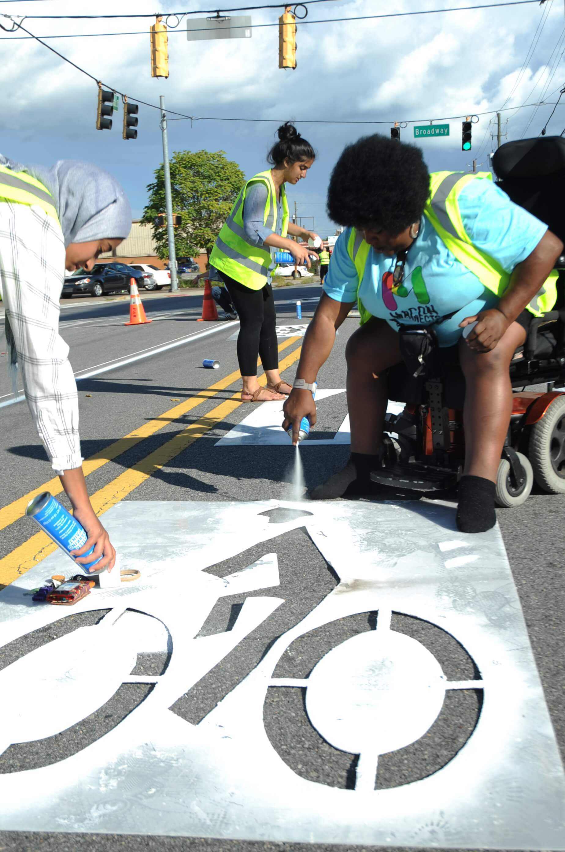 Volunteers painting bike lane symbol on city street.