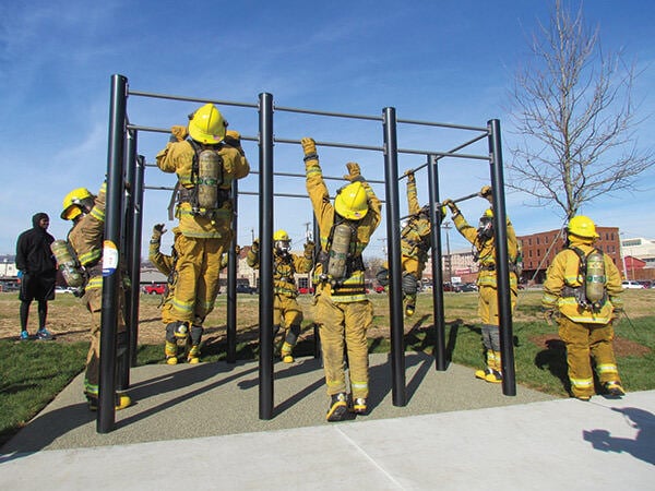 People wearing firefighting equipment using outdoor fitness chin up bars