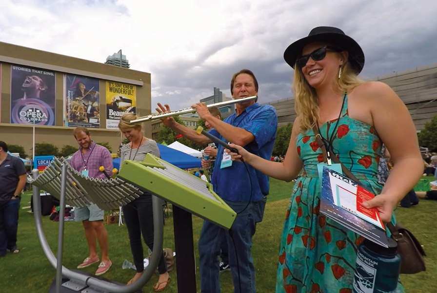 An adult playing a woodwind instrument to accompany the musical instruments installed in the park