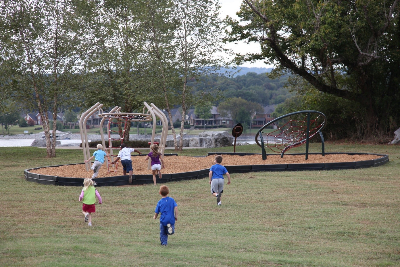 Children running toward nature-themed playground near lake.