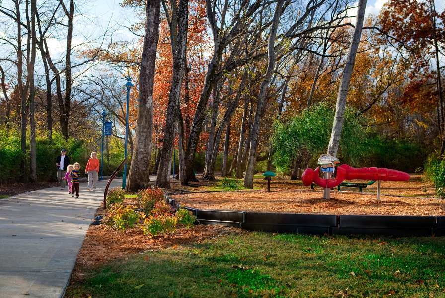 Family walking on wooded trail near nature-themed playground.