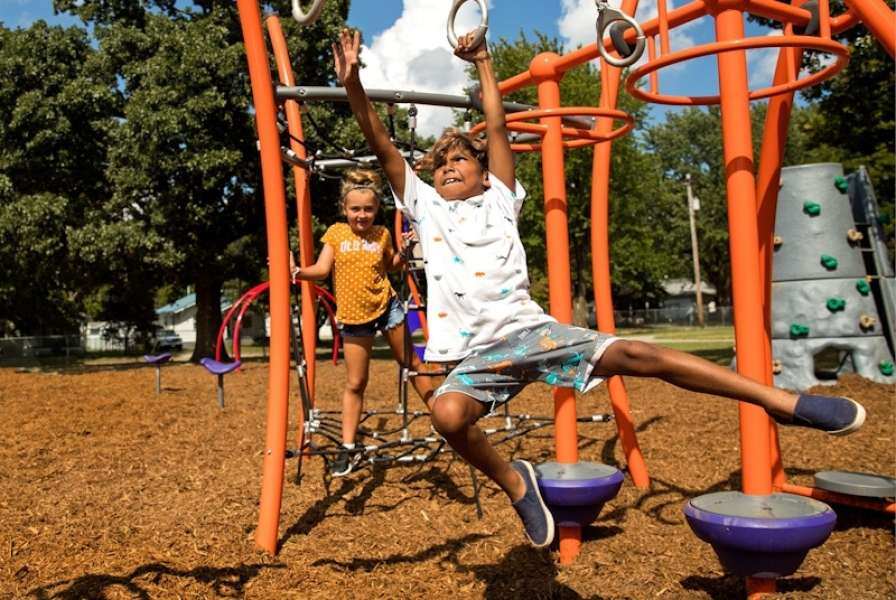 A child reaching for the next still ring on an orange playground