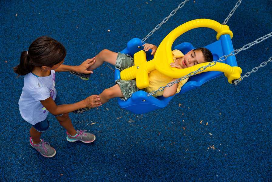 A child pushing another child in an inclusive swing set seat on a playground