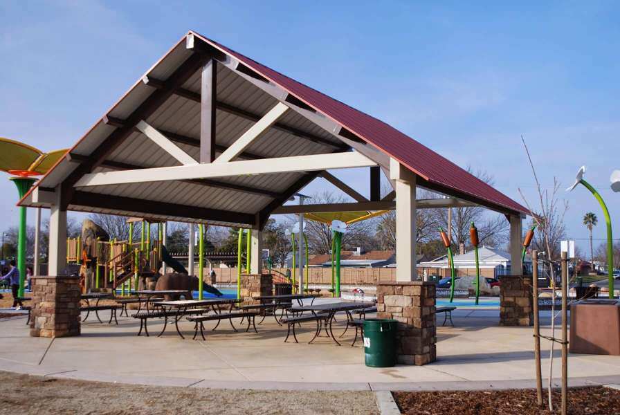 A large rectangular pavilion covering multiple tables and benches next to a playground