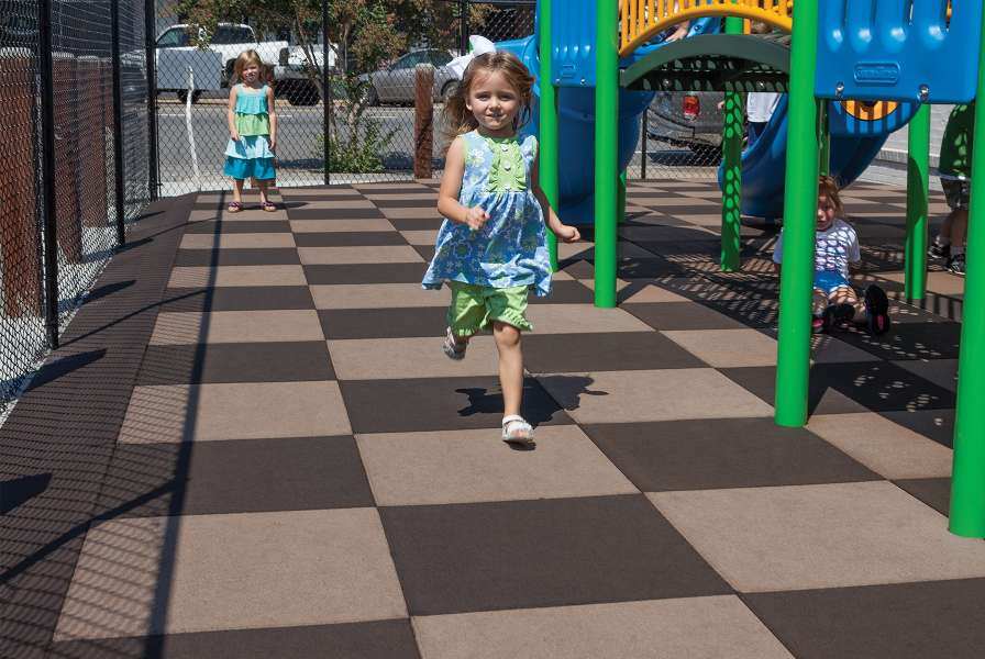 A young girl running on a playground surfaced with rubber tiles