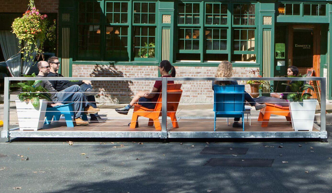 People relaxing on colorful chairs in modern street parklet.