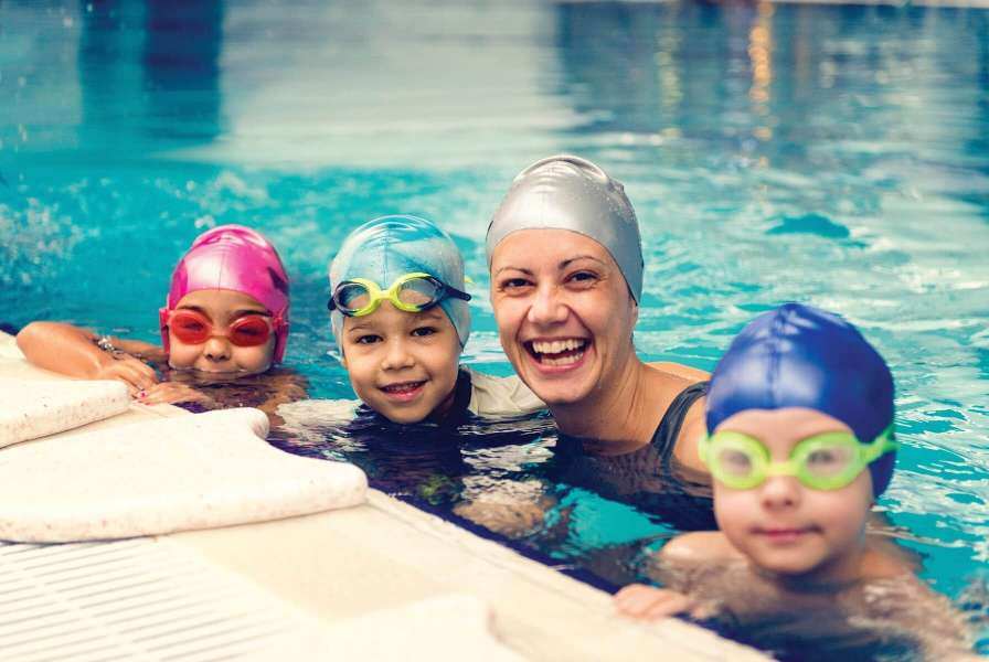 A woman and three children smiling for the camera while wearing goggles and swimming caps