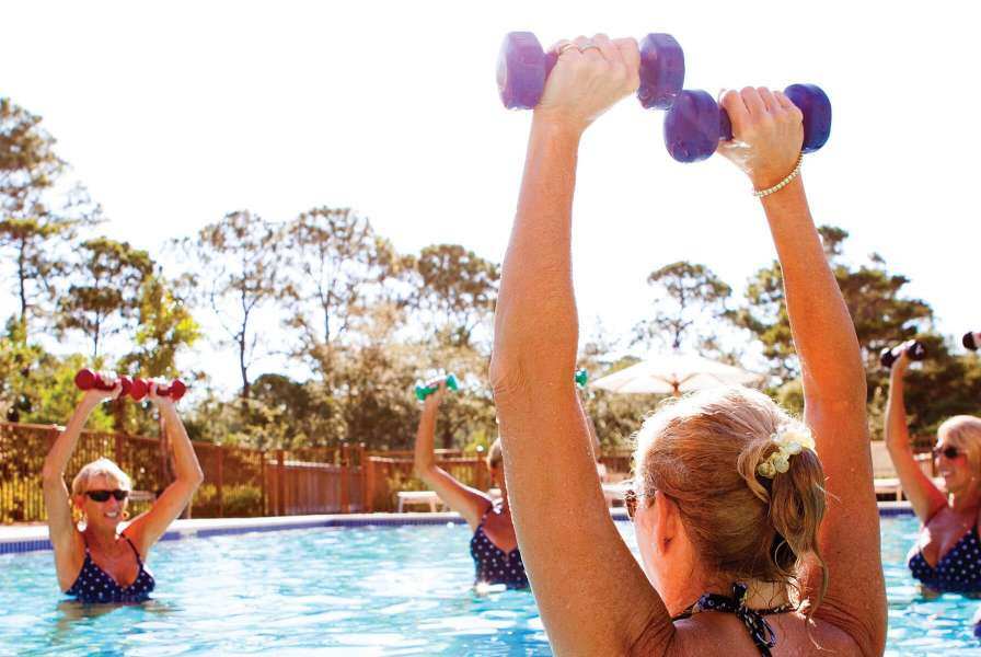Women in a swimming pool lifting weights over their heads
