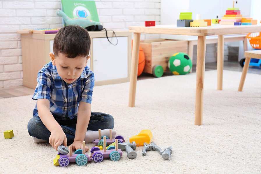 A young boy using a toy wrench to play at tinkering with a toy train
